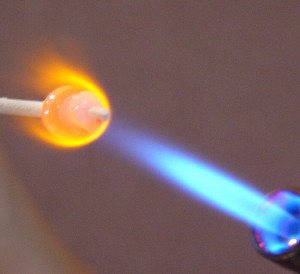 A bead is being formed using a torch in a process called lampworking